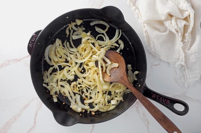 sautéed onions and garlic in a cast iron pan with a wooden spoon