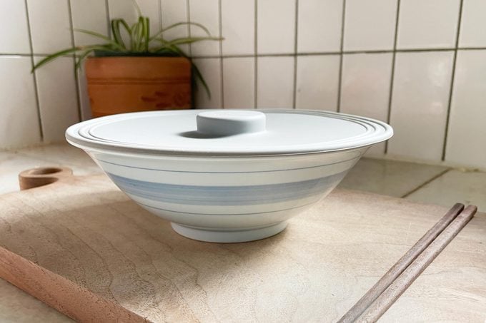 a bowl with a lid on a wooden cutting board in a kitchen