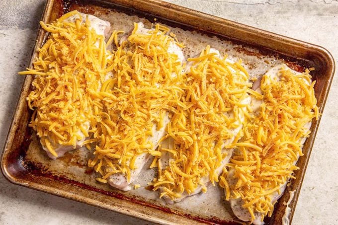 cheesy ranch chicken topped with cheese on a baking sheet before baking