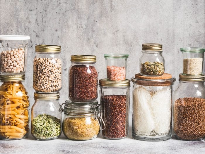 Glass jars with various cereals and seeds - peas split, sunflower and pumpkin seeds, beans, rice, pasta, oatmeal, lentils, bulgur on a grey background