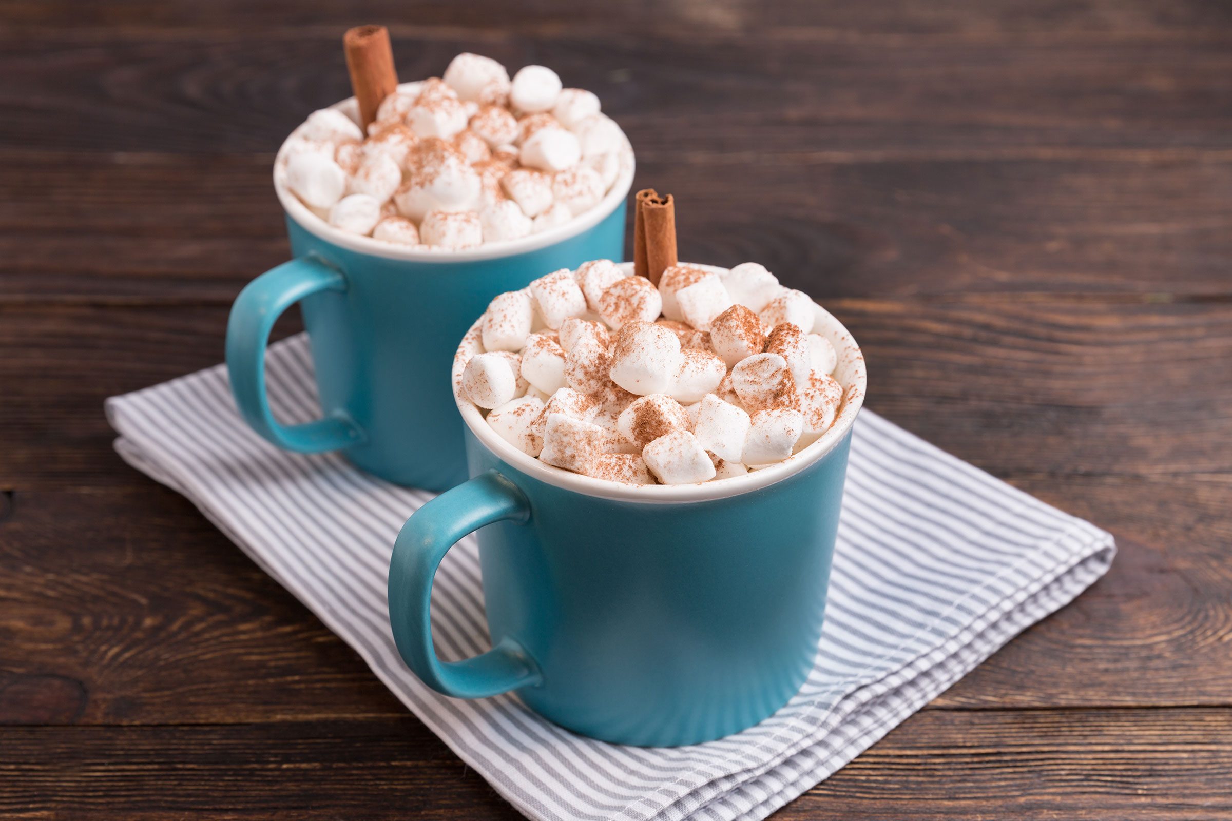Hot Cocoa in blue mugs With Marshmallows On Brown Wooden Background.