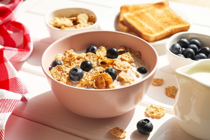 Breakfast of whole wheat flakes with milk, blueberries and toast close-up on wooden table