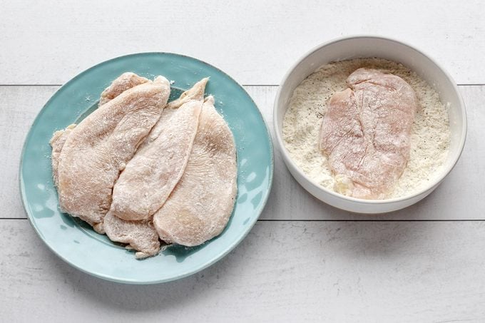 coating raw chicken in a flour mixture