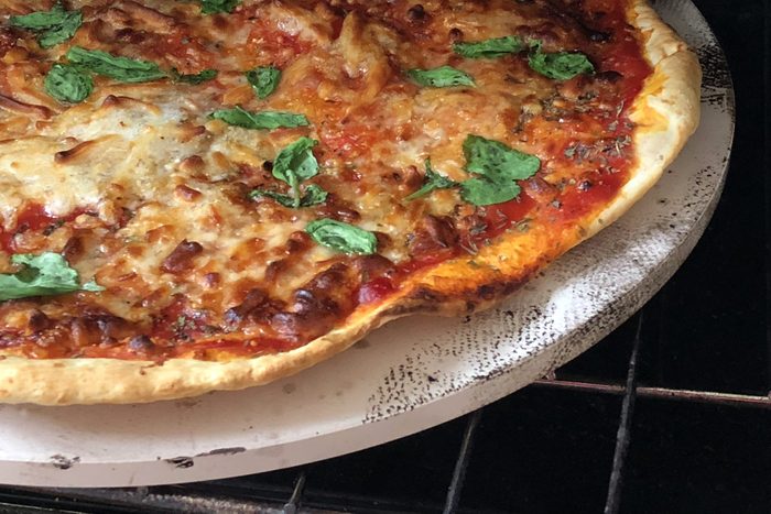 Image of cooked homemade pizza recipe baked in kitchen oven, cooked on pizza stone for thin and crispy base, Italian flag Neapolitan margherita / margarita pizza, grated mozzarella cheese topping, tomato sauce, Italian herbs, fresh basil leaves on top