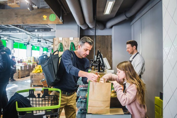 Father and daughter packing groceries in paper bag at checkout counter