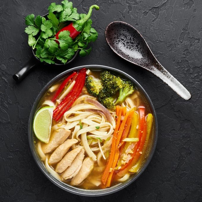 Chicken Thukpa in black bowl at dark slate background. Chicken Thukpa is Tibetan cuisine noodle soup with vegetables and chicken meat. Top view. Copy space