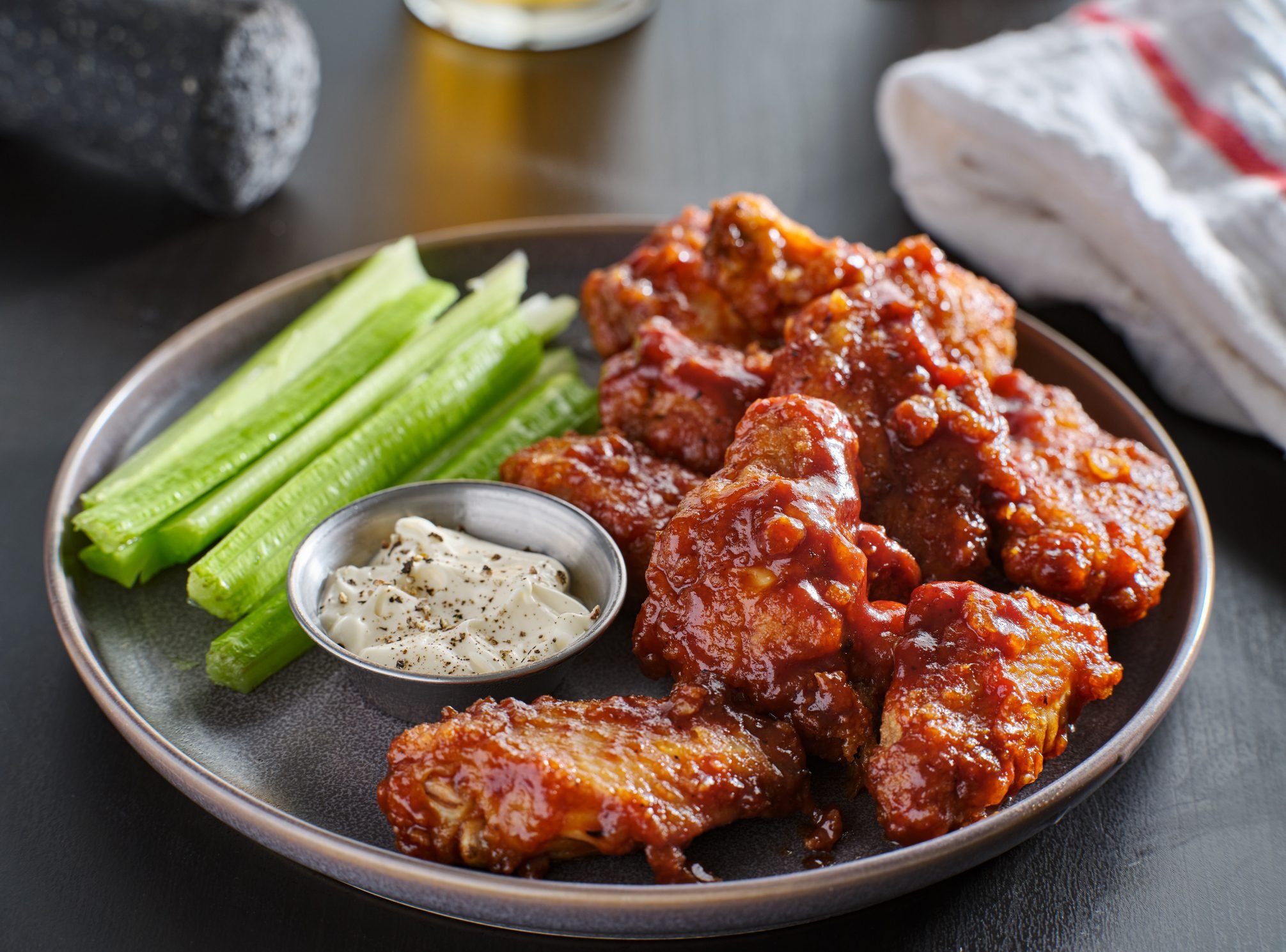 boneless chicken wings covered in honey garlic bbq sauce with ranch and celery on a table with a beer out of focus