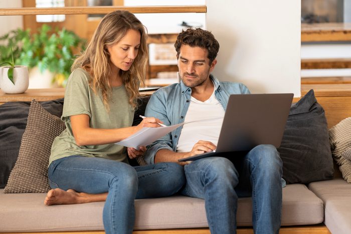Girlfriend signing papers by man with laptop sitting on couch at home