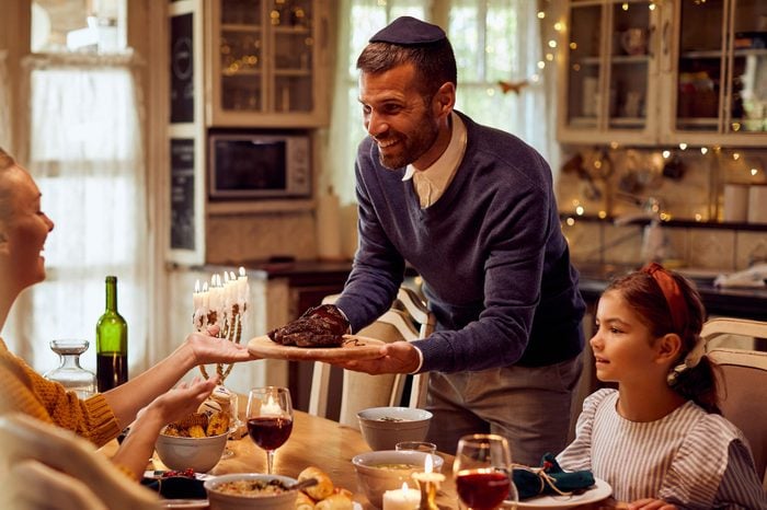 Happy Jewish father serving food to his family while celebrating Hanukkah at dining table.