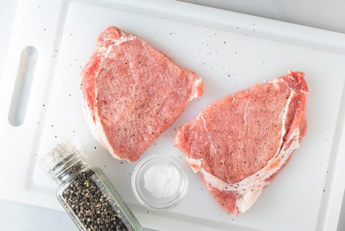 Raw pork chops with salt and black pepper close up on cutting board, flat lay