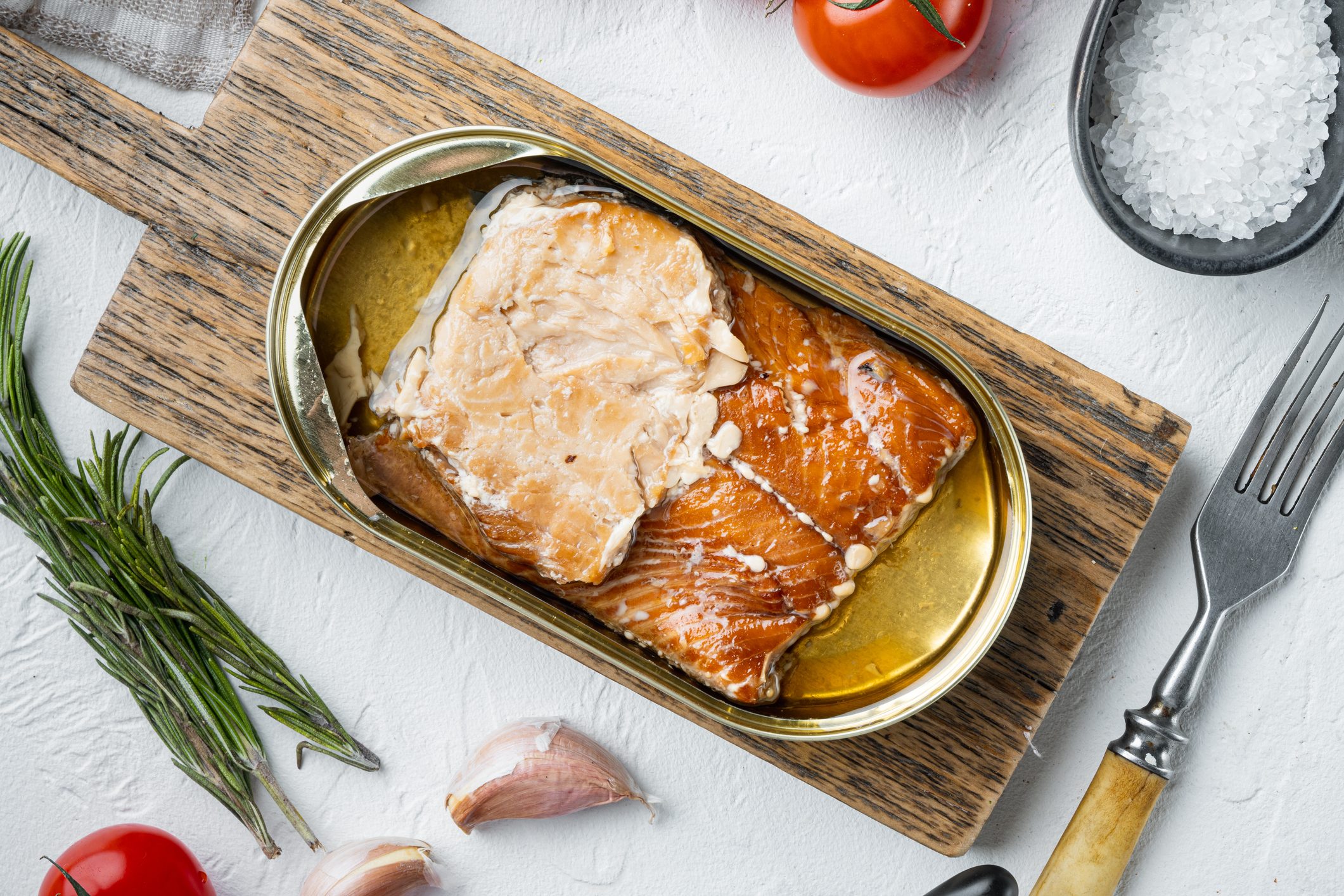 Pink Salmon Canned smoked fish, on wooden cutting board, on white background with herbs and ingredients, top view flat lay