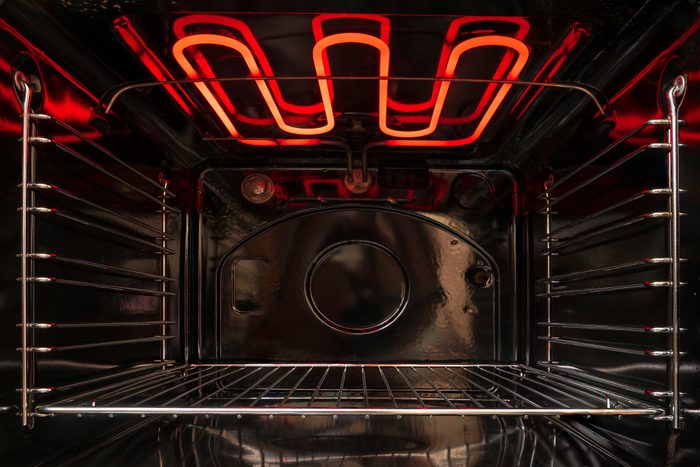 Looking inside the black empty kitchen oven. There is a lattice shelf and a red hot heating element. Background.