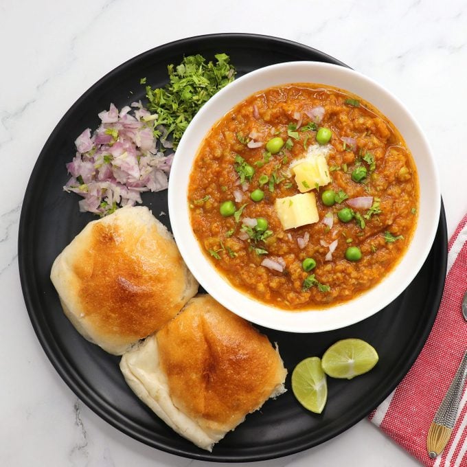 Indian Mumbai Street style Pav Bhaji, garnished with peas, raw onions, coriander, and Butter. Spicy thick curry made of out mixed vegetables served with pav over white background with copy space.