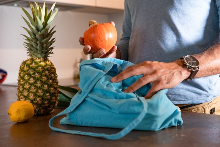 Closeup of a man putting fruit out of a blue shopping bag.