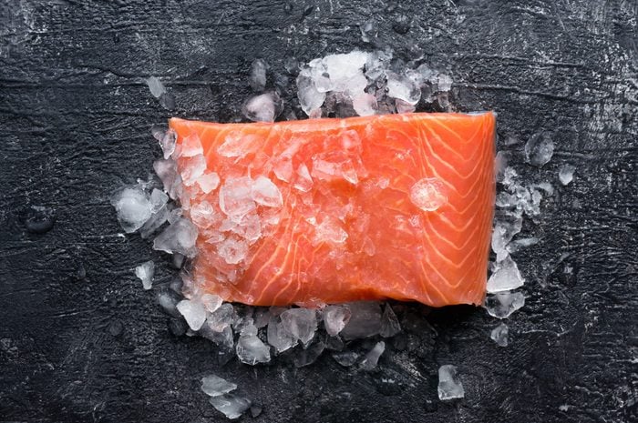 Fresh salmon fillet on ice. Dark slate background. Top view.