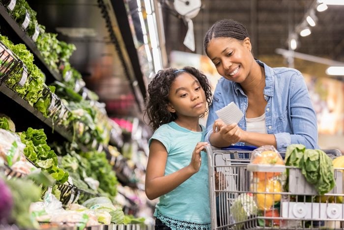 Mother and daughter grocery shop together using a shopping list in the produce section of the supermarket