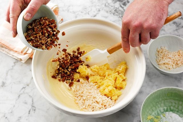 mixing together pineapple, coconut and pecans in a white mixing bowl