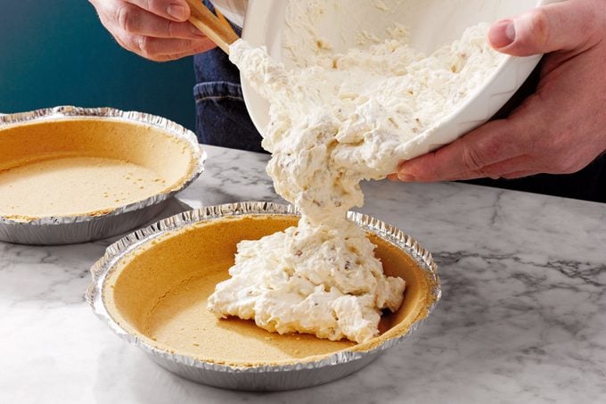 pouring filling into a pie crush in a tin pie dish