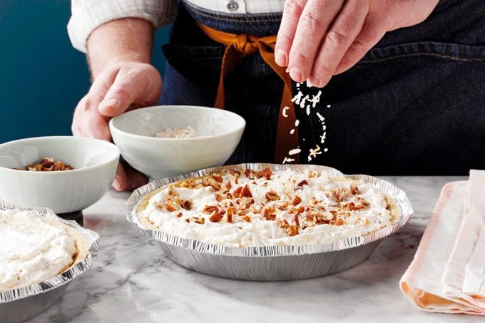 a hand sprinkling topping onto a finished million dollar pie in a tin pie dish 