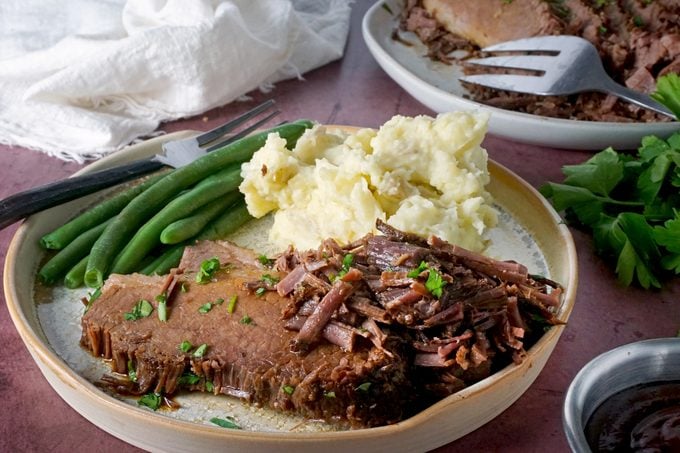 brisket on a plate with mashed potatoes and green beans