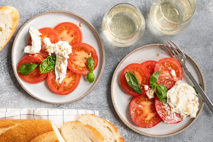 Top view of two plates with Burrata Caprese and a baguette to the side