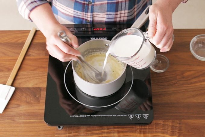 top view of hands pouring milk into a pan on a hot plate and stiring