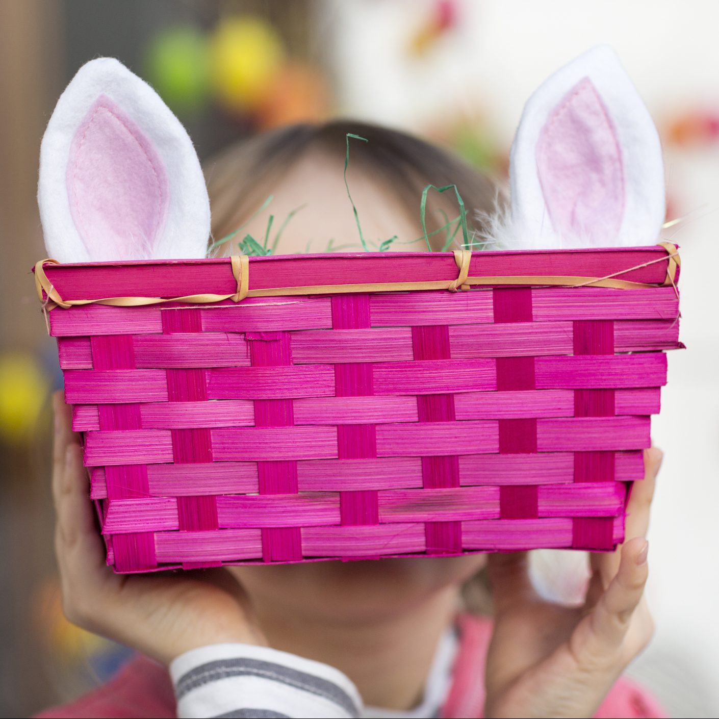 Child hiding face behind pink Easter basket and rabbit ears