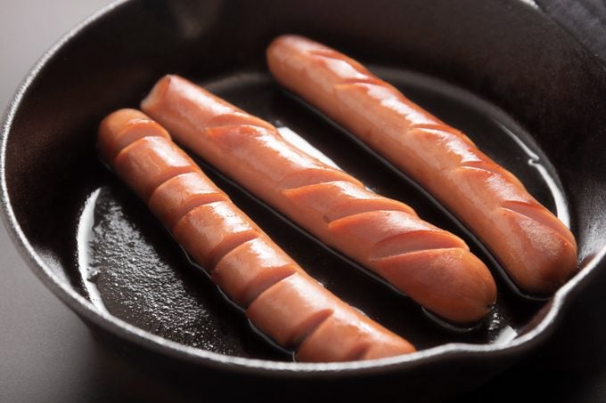 hot dogs in frying pan over dark background isolated. Cooking breakfast hot dogs.