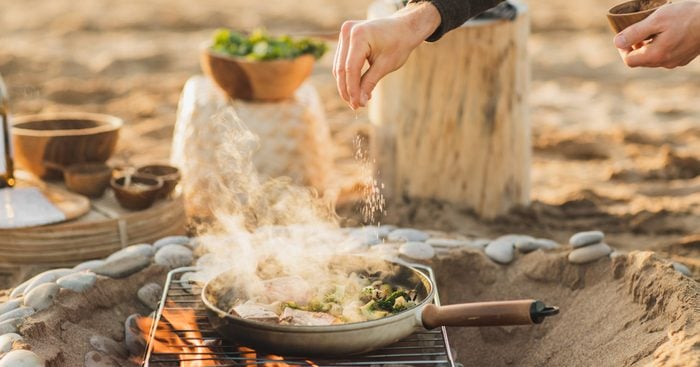 Mans chefs hand sprinkling salt on freshly cooked salmon and vegetables.