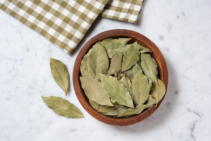 Bay Leaves in a small wood bowl on a counter with a checkered napkin to the side