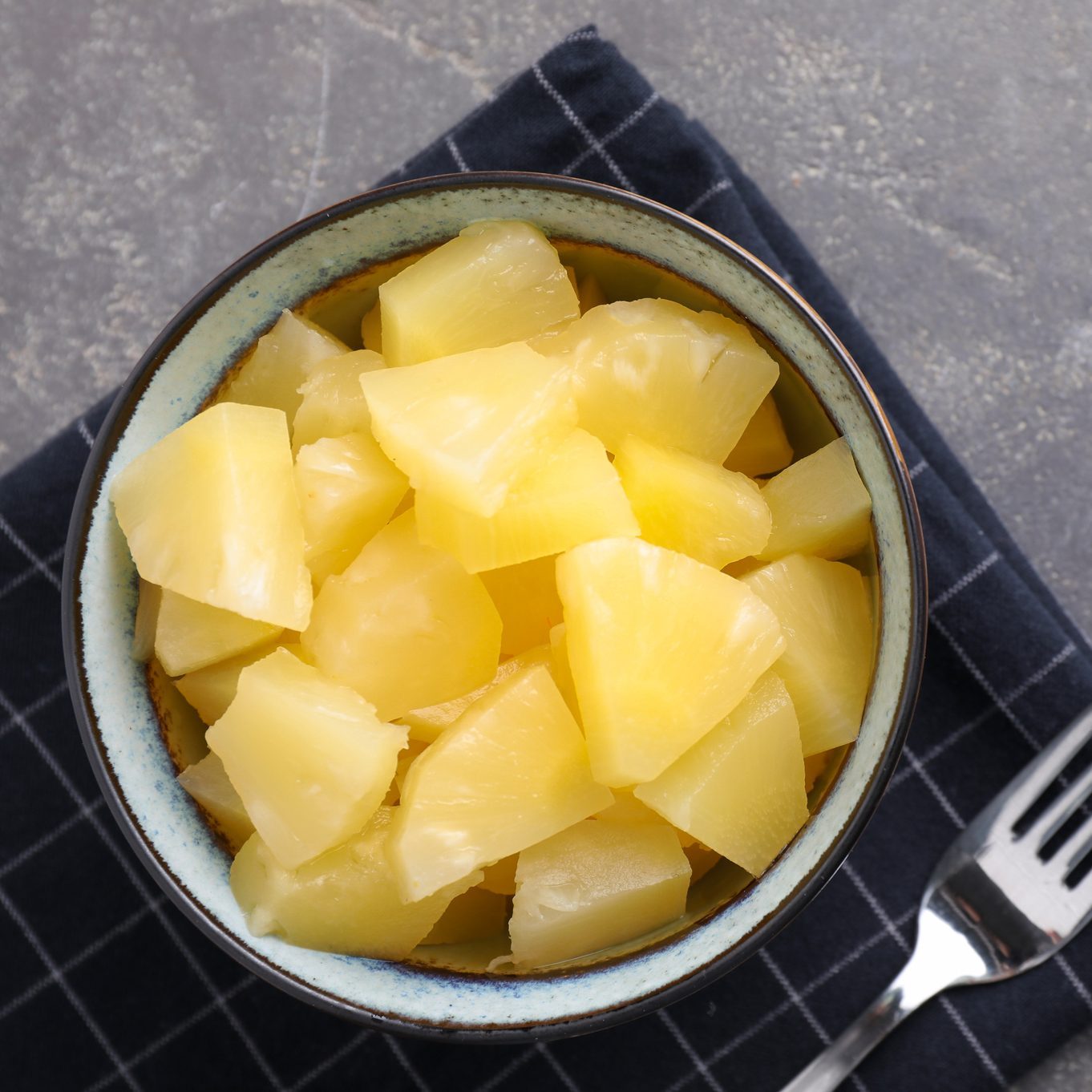 Tasty canned pineapple in bowl on grey table, flat lay