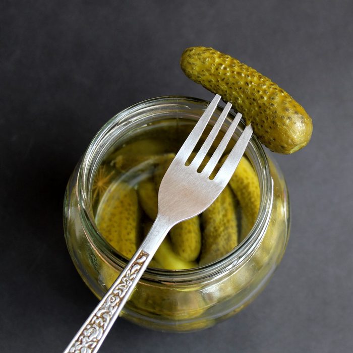 On a black background is a jar of pickled cucumbers and a fork.