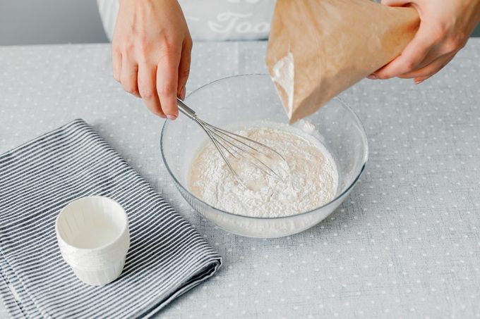 A woman pours gluten-free flour into a glass bowl. The process of preparing healthy pastries. Gluten free diet