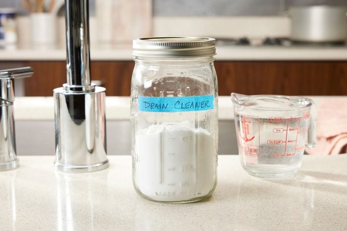 Labled Container With homemade Drain cleaner Mixture next to Boiling Water in a measuring cup on the edge of a kitchen sink