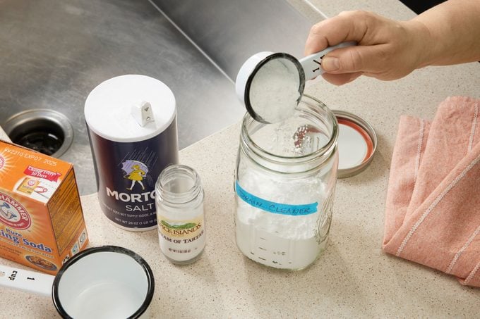 Hands Adding Baking Soda Salt And Cream Of Tartar To A Jar near a kitchen sink