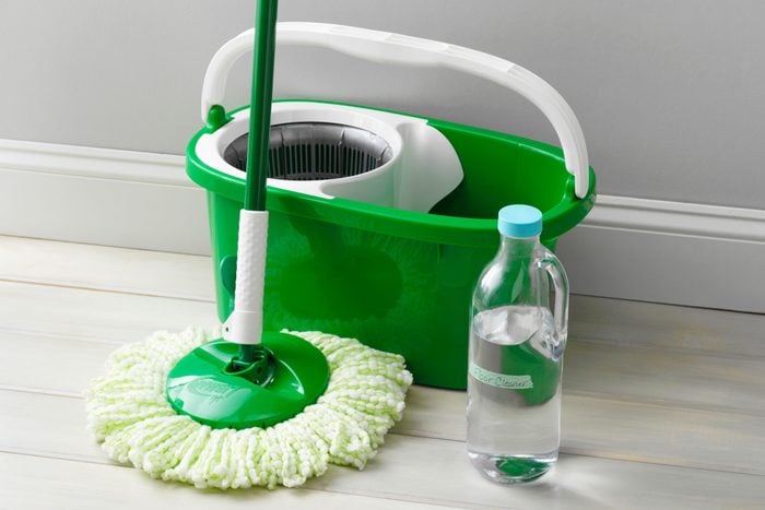 Homemade floor cleaner in a bottle arranged near a wall next to a mop and bucket