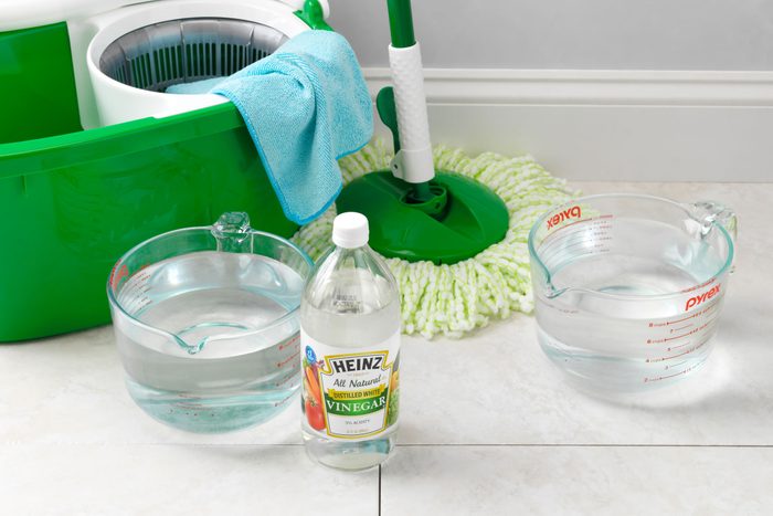 cleaning supplies for a homemade tile floor cleaner arranged on a tile floor near the wall