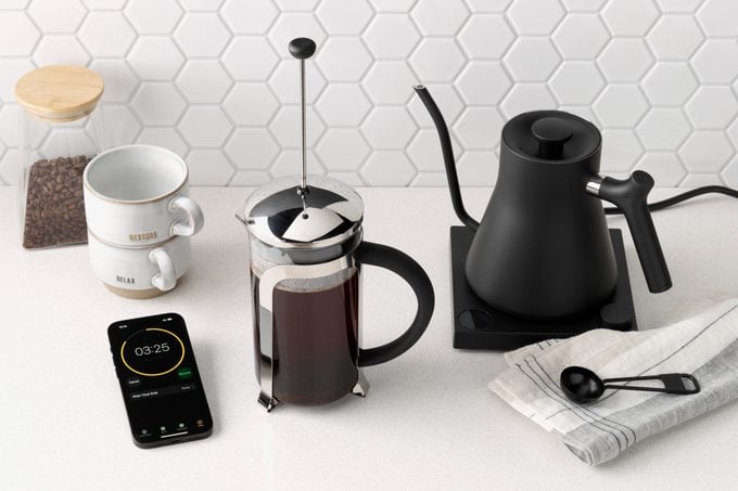 a phone with a timer next to a French press coffee maker and a goose neck kettle