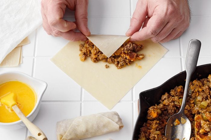 rolling an egg roll on a white tile kitchen counter