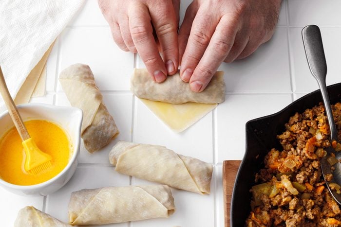 rolling an egg roll on a white tile kitchen counter