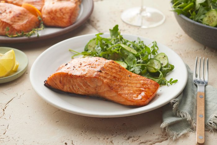 marinated and grilled salmon on a white plate with a side of greens