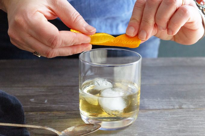 squeezing orange peel into a glass with ice for a Tequila Old Fashioned