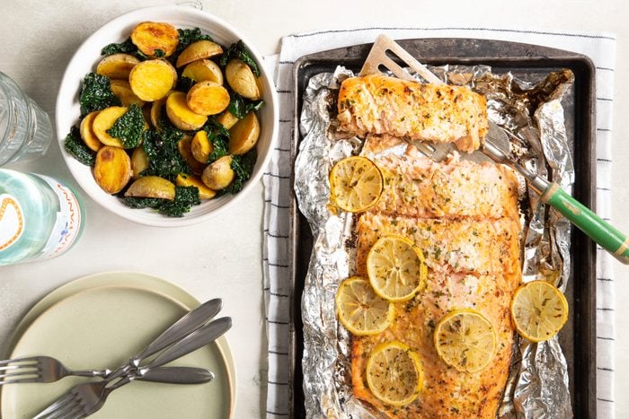 salmon in foil with lemon slices on a baking sheet with a side of potatoes in a bowl