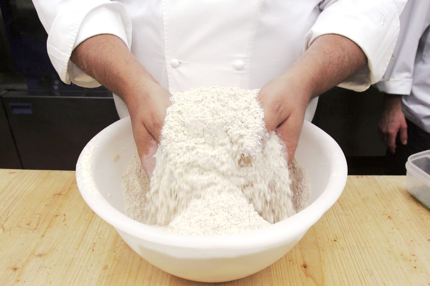 Italian Chef tosses flour in a mixing bowl while teaching a technical course on local cuisine