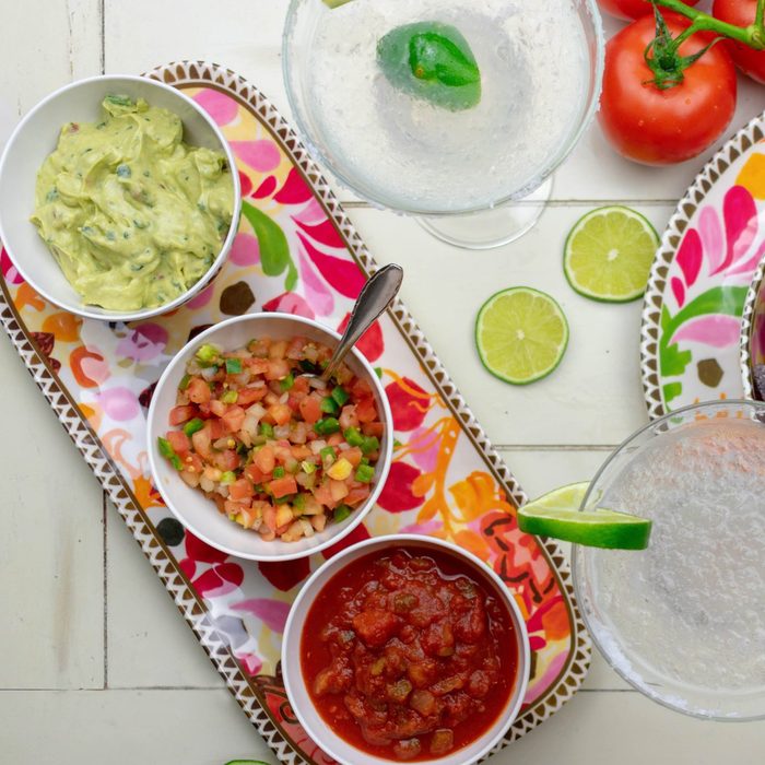 Mexican food flat lay - top view of chips, salsas, fresh ingredients and margaritas