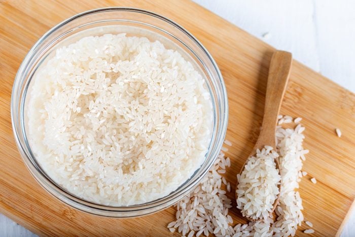 Soaked rice, grain, cloudy liquid water in glass bowl on wooden background
