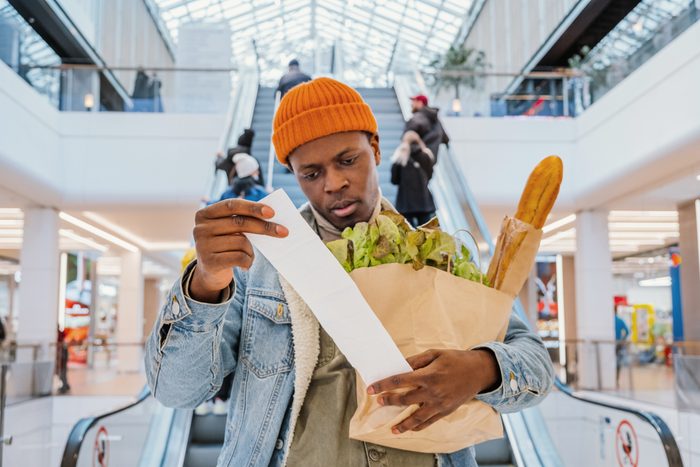 Surprised black man looks at receipt total with food in mall