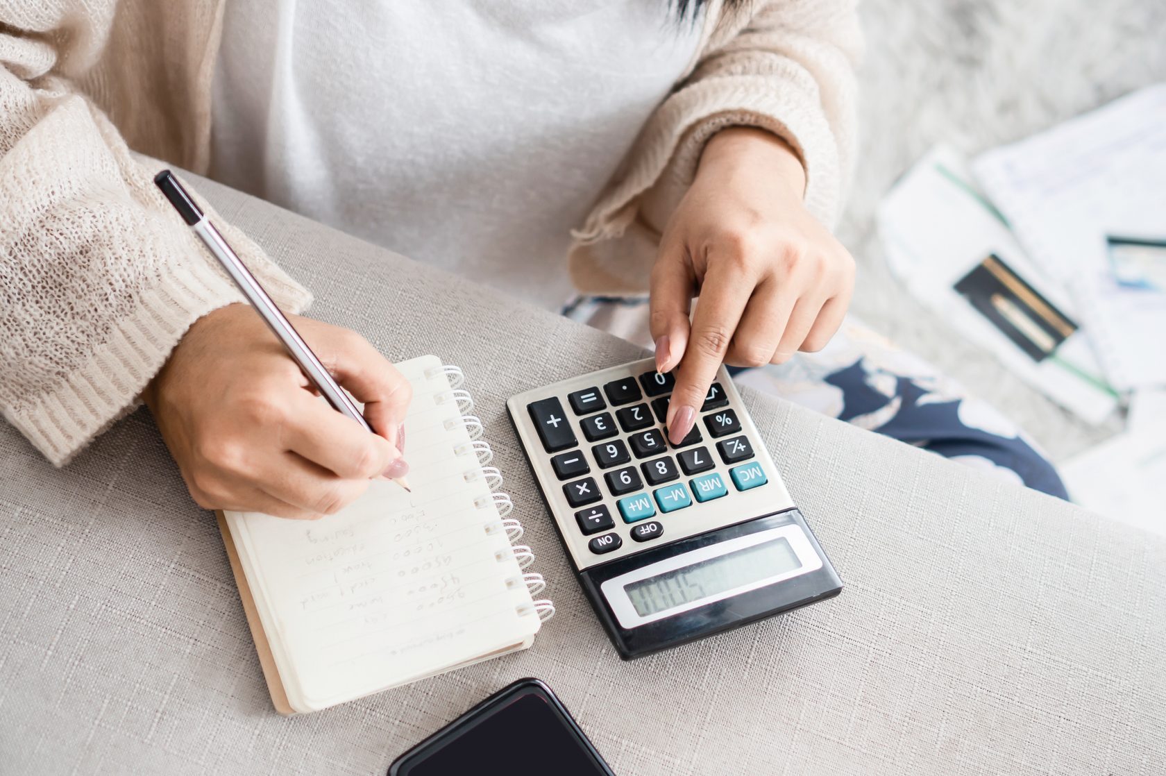woman writing a list of debt on notebook calculating her expenses with calculator