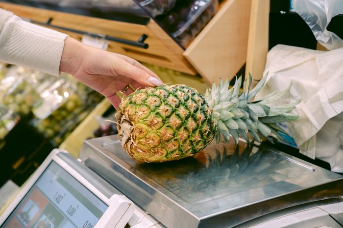Woman weighs pineapple on scale in supermarket