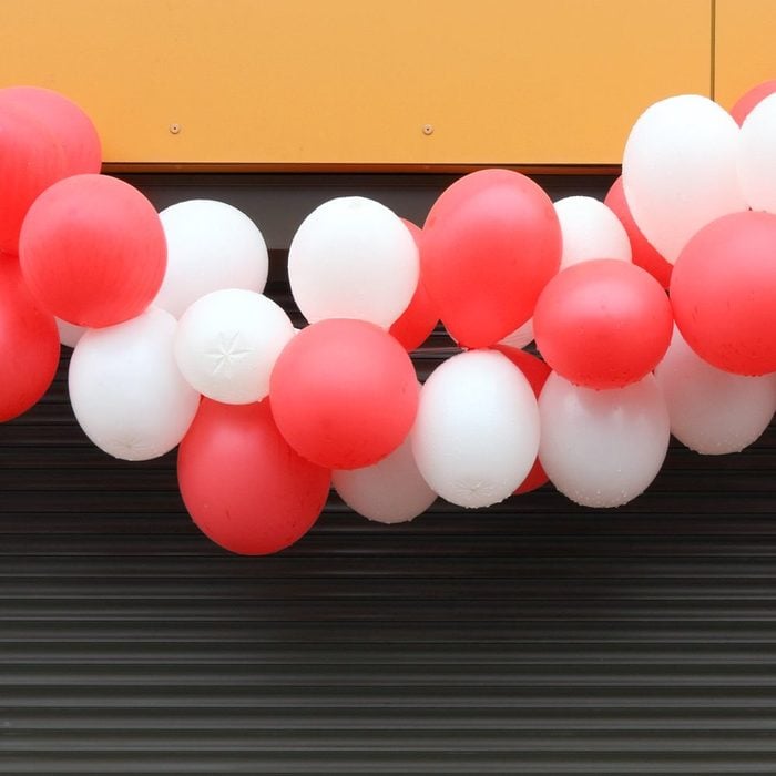The garland of white and red balloons hangs over the window closed by brown blinds.Rainy day